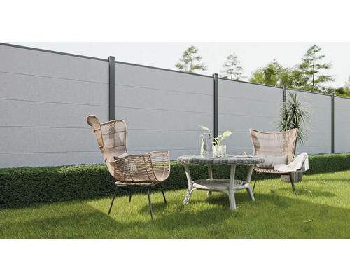 Scène de jardin avec clôture en béton, fauteuils en rotin et table ronde sur une pelouse.