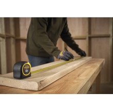 Artisan mesurant une planche de bois avec un mètre ruban Stanley Fatmax, longueur 5 mètres.