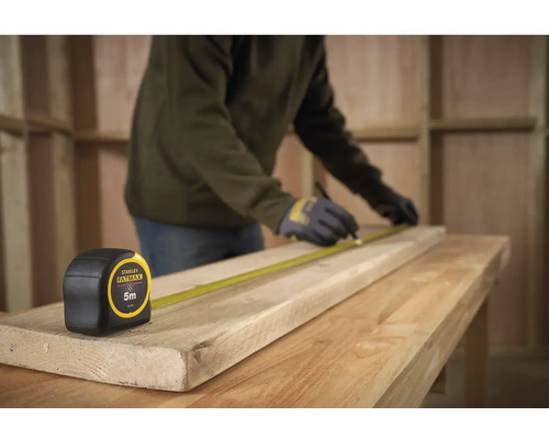 Artisan mesurant une planche de bois avec un mètre ruban Stanley Fatmax, longueur 5 mètres.