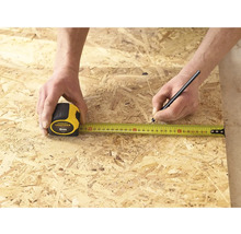 Une personne mesure un morceau de bois avec un mètre ruban Stanley Fatmax de 5 mètres et le marque avec un crayon.