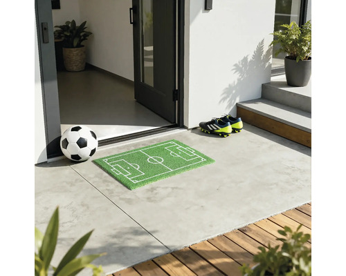 Fußball vor einer Haustür mit Fußballfeld Fußmatte und Fußballschuhen.