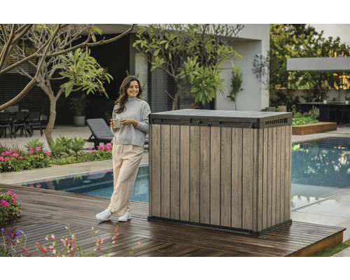 Garten-Aufbewahrungsbox aus Holzoptik neben einer Frau auf einer Terrasse