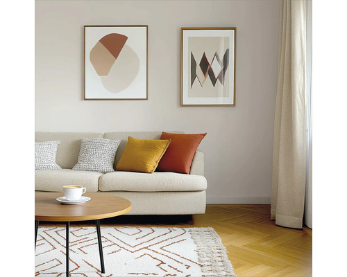 Wohnzimmer mit Sofa, Kissen, Couchtisch, Teppich und zwei gerahmten Bildern an der Wand