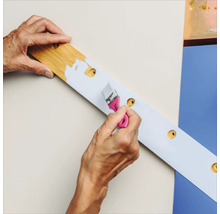 Eine Person streicht ein Holzbrett mit einer Bohrmaschine mit Farbe.