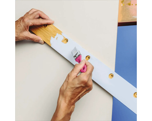 Eine Person streicht ein Holzbrett mit einer Bohrmaschine mit Farbe.