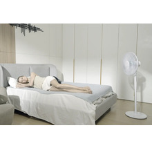 Femme dormant sur un lit avec un tapis de refroidissement à côté d'un ventilateur sur pied