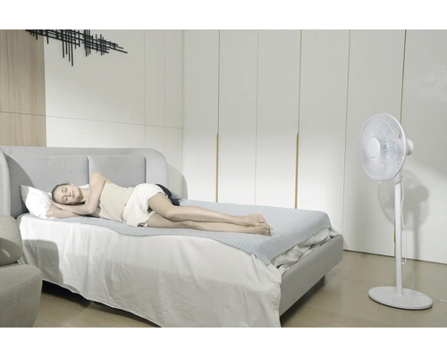 Femme dormant sur un lit avec un tapis de refroidissement à côté d'un ventilateur sur pied