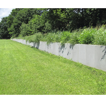 Lange, graue Betonstützmauer auf Rasenfläche mit Bewuchs oben