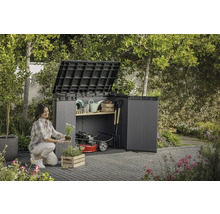 Eine Frau pflanzt Blumen vor einem offenen Gartenschrank mit Gartengeräten