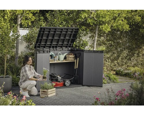 Eine Frau pflanzt Blumen vor einem offenen Gartenschrank mit Gartengeräten