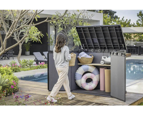 Gartenszene mit einer Frau, die auf eine geöffnete Aufbewahrungsbox auf einer Holzterrasse am Pool zugeht