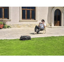 Un robot tondeuse tond la pelouse pendant qu'une personne est assise dans le jardin.