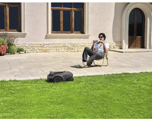 Un robot tondeuse tond la pelouse pendant qu'une personne est assise dans le jardin.