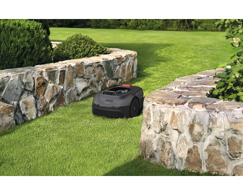Robot tondeuse à gazon sur une pelouse entre deux murs de pierre
