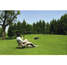 Un homme est assis dans le jardin sur une chaise et commande un robot tondeuse avec son smartphone.