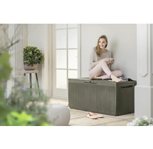 Eine junge Frau sitzt auf einer grauen Aufbewahrungsbox im Freien und hält eine Tasse