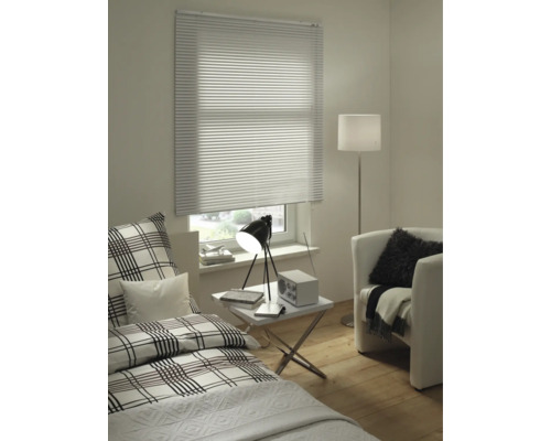 Espace de vie avec lit, fauteuil, lampadaire, table et fenêtre avec stores vénitiens