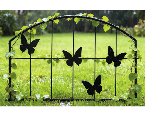 Portail de jardin décoratif avec motifs de papillons et décorations végétales dans le jardin.