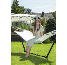 Une femme est assise dans un hamac autoportant dans le jardin et boit une boisson.