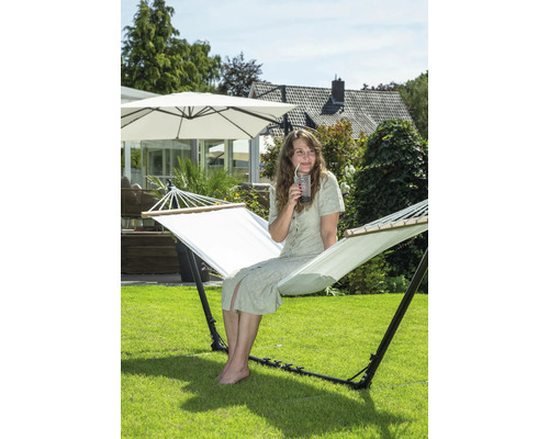 Une femme est assise dans un hamac autoportant dans le jardin et boit une boisson.