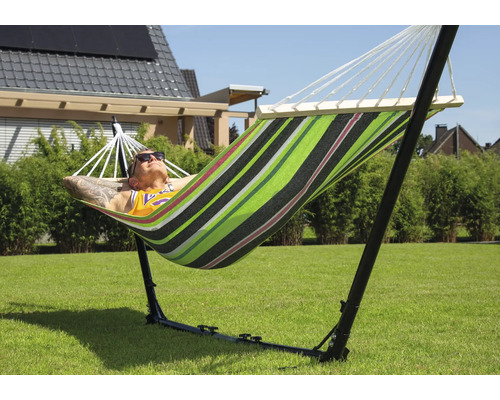 Un homme se détend dans un hamac rayé avec support dans le jardin.