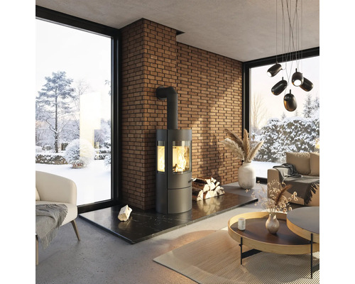 Salon avec poêle à bois, mur en briques et vue sur un paysage enneigé