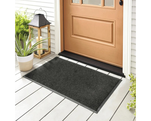 Paillasson gris devant une porte d'entrée sur un porche avec des plantes et un photophore