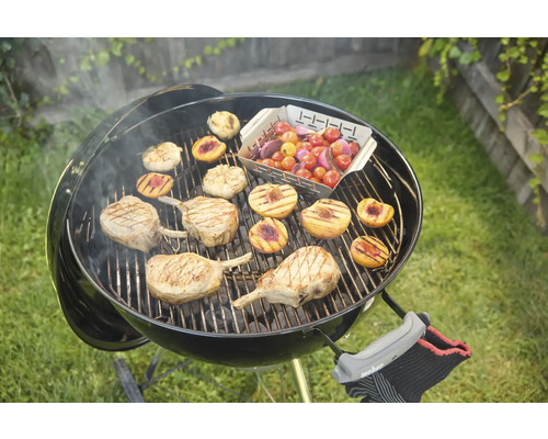Kugelgrill mit Grillgut wie Fleisch, Pfirsichen und Tomaten auf dem Rost