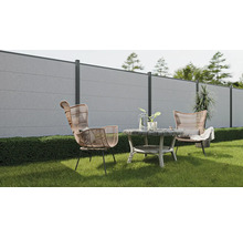 Scène de jardin avec une clôture en béton, deux fauteuils en rotin et une table ronde sur une pelouse.