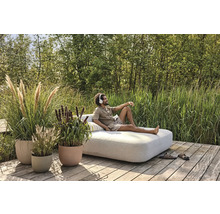 Mann entspannt mit Kopfhörern auf einem Lounge-Sofa im Garten, umgeben von Pflanzgefäßen mit Ziergräsern.