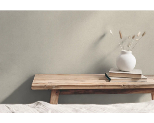 Dekorative Szene mit Holzbank, Büchern und Vase mit Gräsern vor einer Wand.