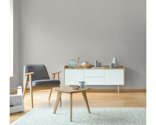 Wohnzimmer mit Sessel, Tisch und Sideboard vor einer grauen Tapete