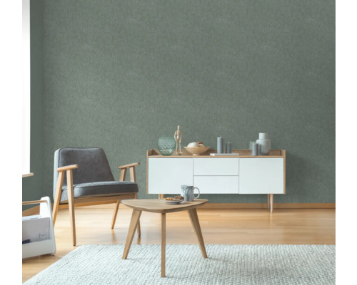 Wohnzimmer mit grüner Struktur-Tapete, Sessel, Tisch und Sideboard