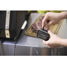 Un homme connecte un thermomètre de barbecue à un morceau de viande posé sur une planche à découper.