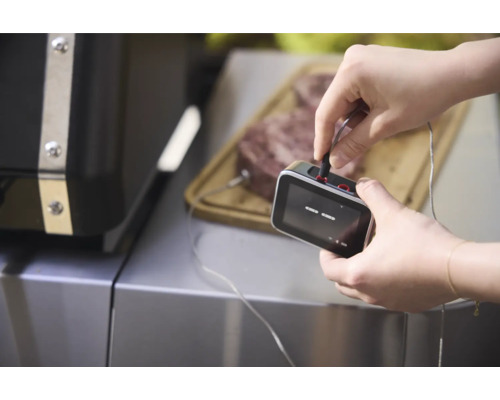 Un homme connecte un thermomètre de barbecue à un morceau de viande posé sur une planche à découper.