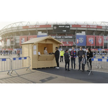 Cabane en bois comme stand de vente devant un stade de football avec des personnes