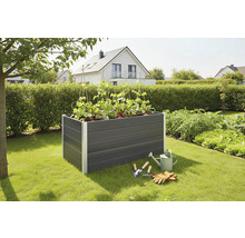 Hochbeet aus Kunststoff mit Pflanzen, Gießkanne und Gartenwerkzeugen im Garten.