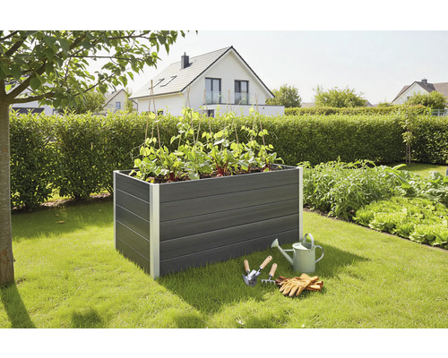 Hochbeet aus Kunststoff mit Pflanzen, Gießkanne und Gartenwerkzeugen im Garten.