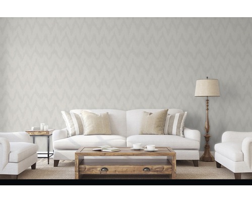 Salon avec papier peint à motifs en zigzag, canapé, fauteuils, table et lampadaire pour une atmosphère lumineuse et accueillante.