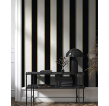 Vue d'une pièce avec du papier peint rayé noir, blanc et doré, ainsi qu'une étagère avec des livres et une lampe.