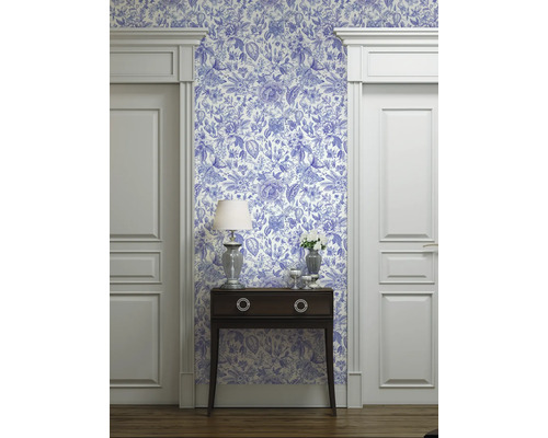 Vue d'une pièce avec du papier peint à motifs bleus et blancs, une commode, une lampe et des encadrements de porte