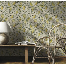 Pièce décorative avec un papier peint à motifs de citrons et de branches d'olivier, une table en bois, une lampe, un livre et une chaise en rotin.