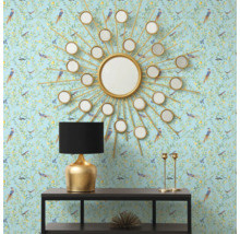 Intérieur décoratif avec un miroir rond en forme de soleil, une lampe de table et une console devant un papier peint à motifs.