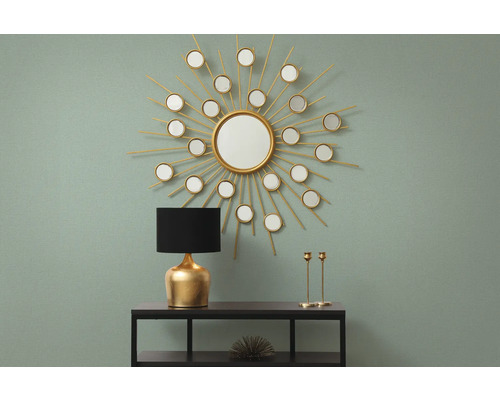 Intérieur décoratif avec miroir en forme de soleil, lampe et chandeliers sur une étagère.