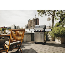 Grill en acier inoxydable sur un toit-terrasse à côté d'une table et de chaises en bois.