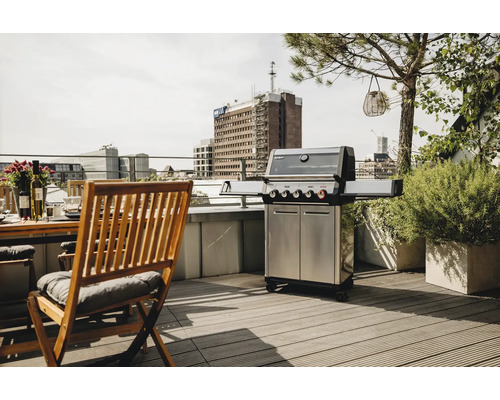 Grill en acier inoxydable sur un toit-terrasse à côté d'une table et de chaises en bois.