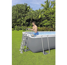 Un homme entre dans une piscine tubulaire rectangulaire dans un jardin en utilisant une échelle.