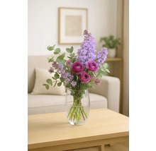 Arrangement floral composé de lilas mauve et de roses dans un vase en verre sur une table