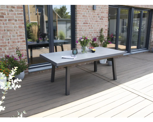 Scène de jardin avec une table à manger en béton et métal sur une terrasse