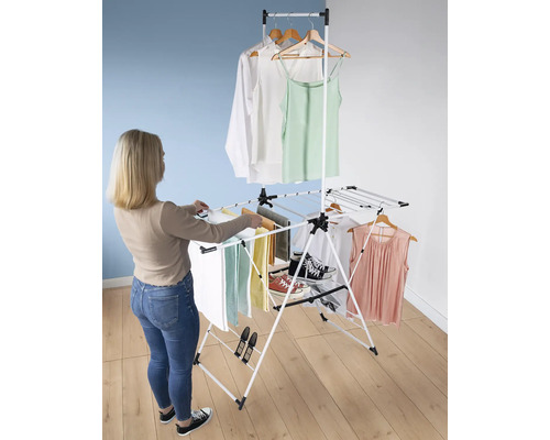 Eine Frau hängt Wäsche auf einem weißen, mehrstöckigen Wäscheständer mit Kleidung und Handtüchern.